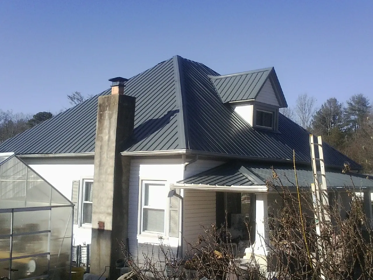 Dark blue standing seam metal roof on a white farmhouse with dormer — Slate & Tile Roof Repair by Roofing Brothers in Blackwell
