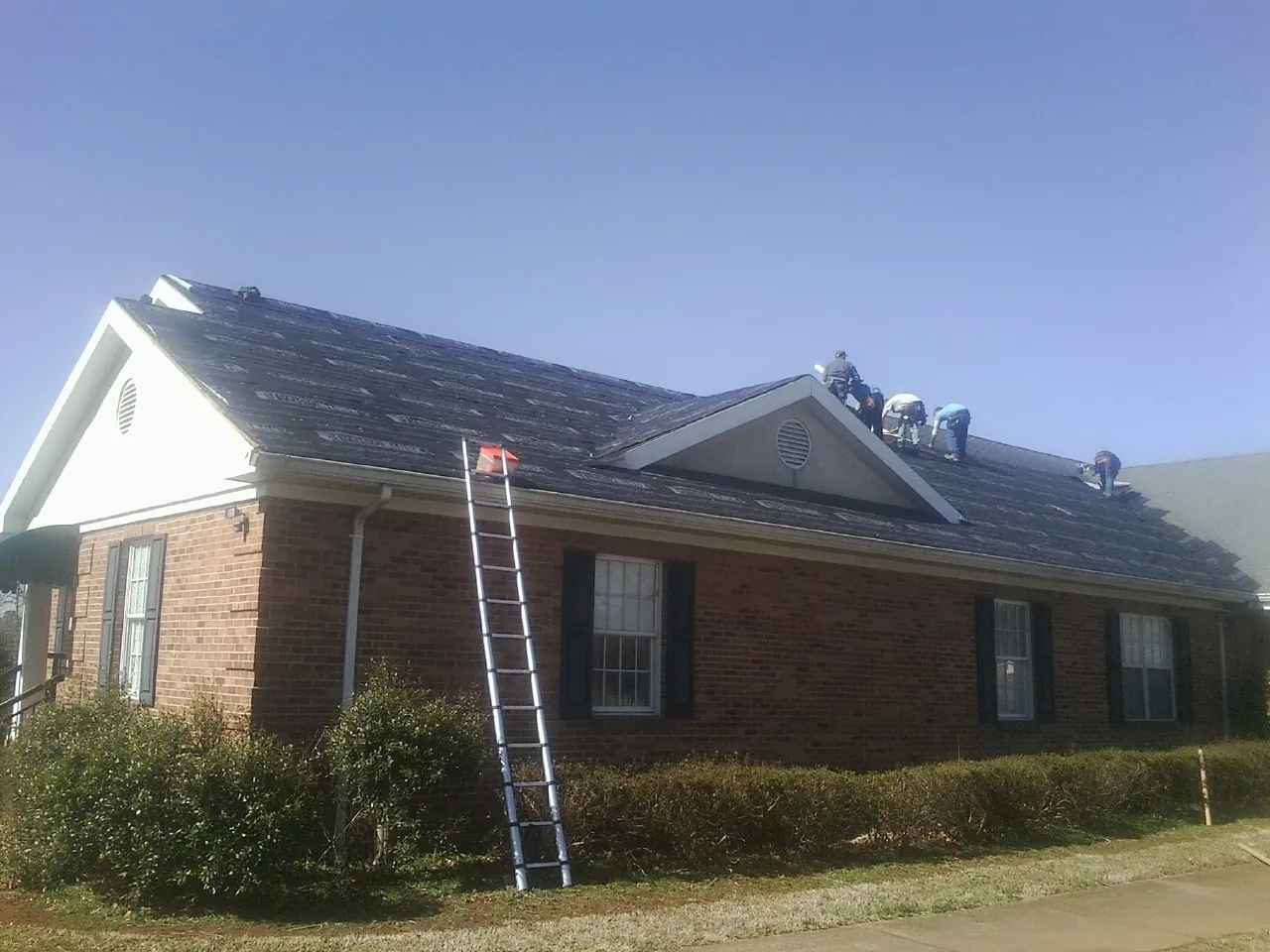 Crew tearing shingles off a brick ranch roof with a ladder set — Emergency Roof Repair work by our crew in Blackwell
