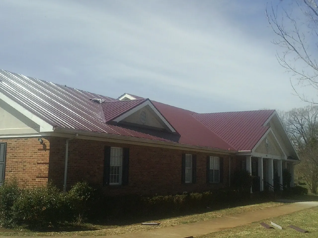 Red metal roof with gabled entries on a long brick building, from a Hail Damage Roof Repair job in Blackwell