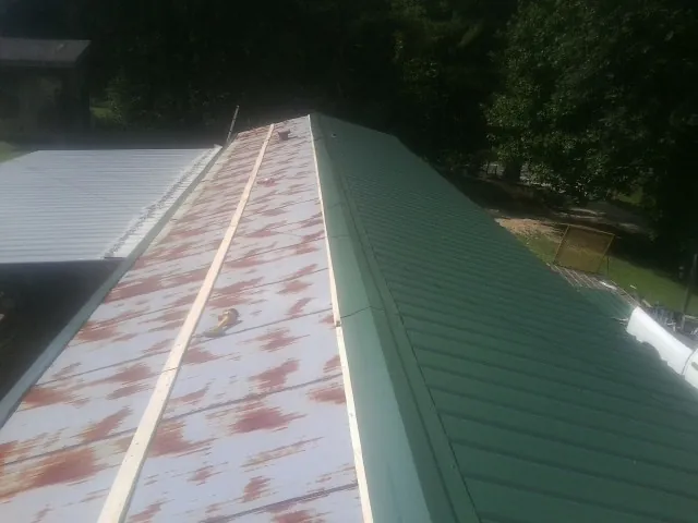 Old rusted panels beside newly installed green metal roofing — Wind Damage Roof Repair by Roofing Brothers in Blackwell