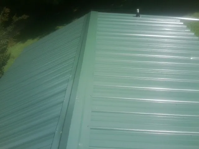New green metal panels meeting at the ridge of a roof — Flat Roof Repair work by our crew in Blackwell