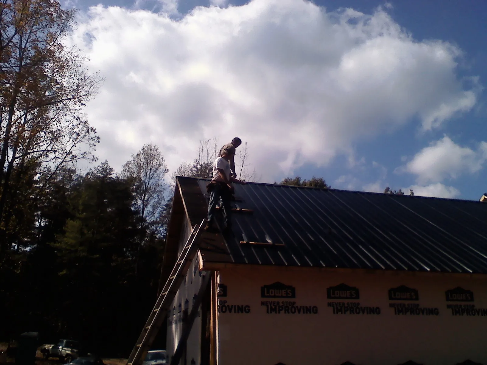 Roofer fastening dark metal panels high against a cloudy sky, from a Roof Inspection job in Blackwell