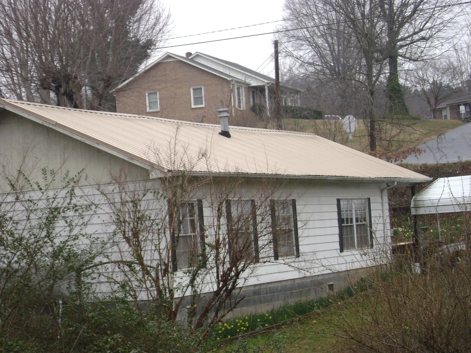 Tan metal roof on a white sided house set into a hillside — Commercial Roofing by Roofing Brothers in Blackwell