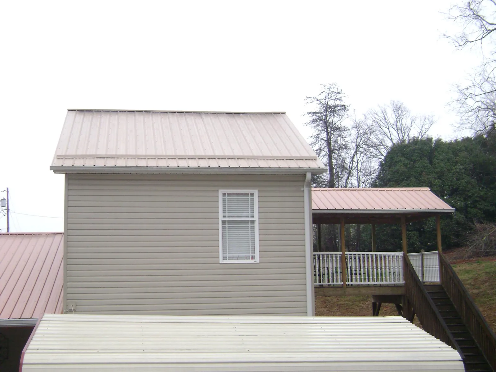 Tan metal roofs on a two story addition and attached porch, from a Roof Replacement job in Blackwell